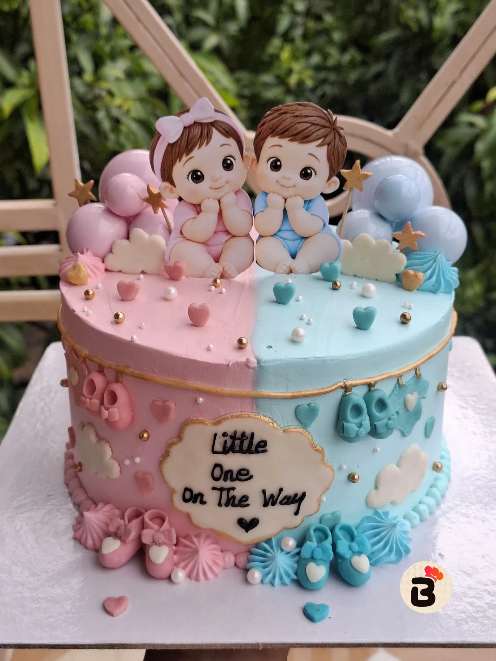 A pink and blue baby shower cake decorated with a fondant baby topper, balloons, and baby-themed details.