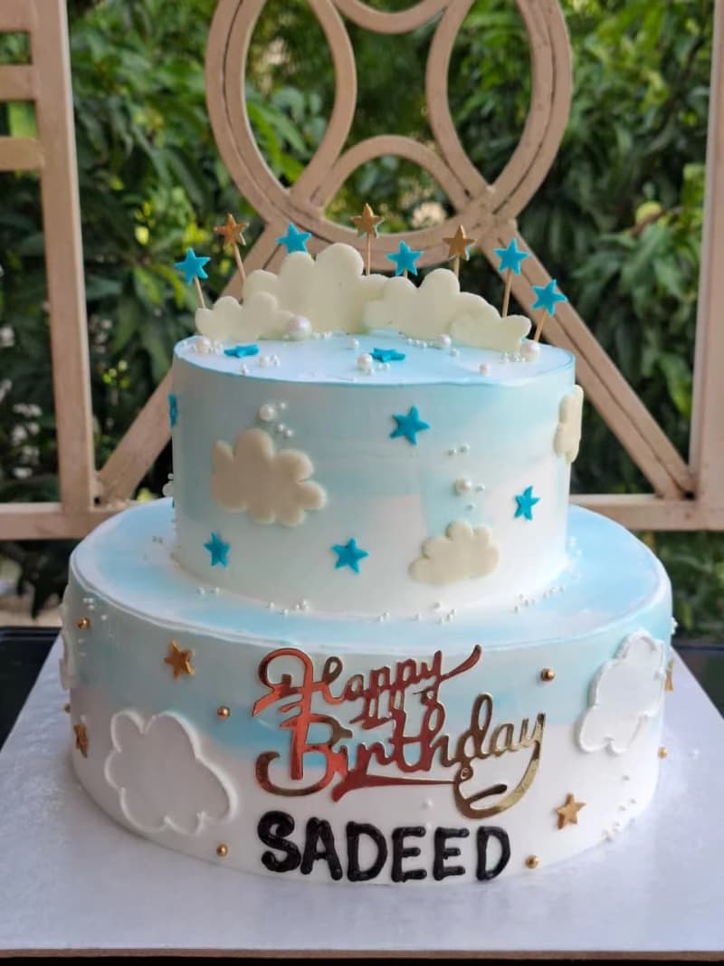 a two tier cloud theme cake for birthday. blue color. clouds are made of chocolate.